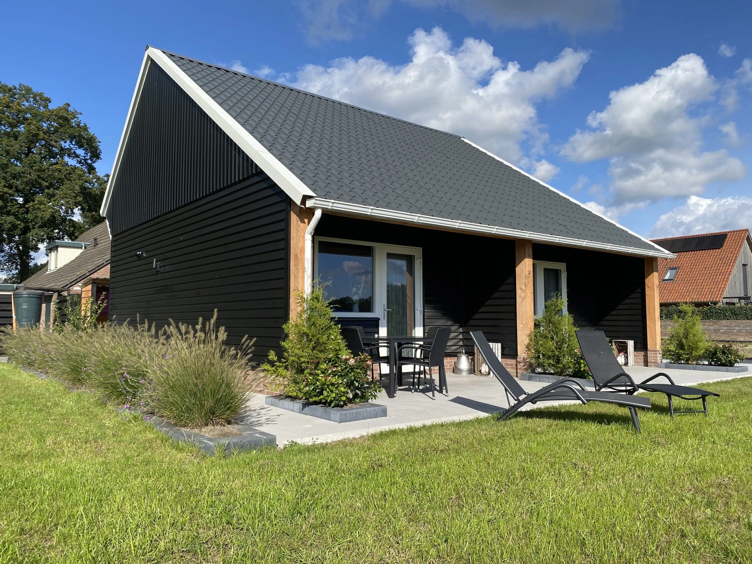 De zwarte kapschuur met twee terrassen op het zuiden en ligstoelen op het gras